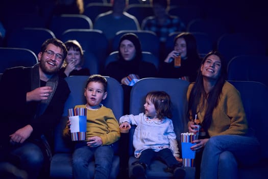 A modern family enjoys quality time together at the cinema, indulging in popcorn while watching a movie with their children.