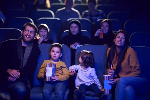 A modern family enjoys quality time together at the cinema, indulging in popcorn while watching a movie with their children.