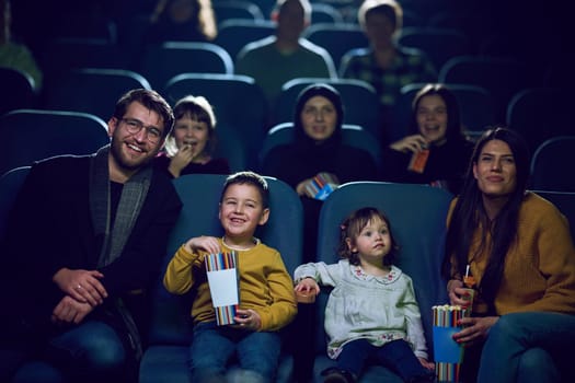 A modern family enjoys quality time together at the cinema, indulging in popcorn while watching a movie with their children.