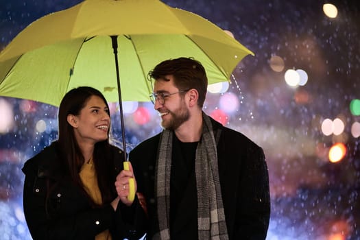 In the romantic ambiance of a rainy night, a happy couple walks through the city, sharing tender moments under a yellow umbrella, surrounded by the glistening glow of urban lights.