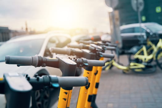 A row of electric scooters parked on the asphalt in front of a car, showcasing the blend of automotive engineering and alternative travel machine