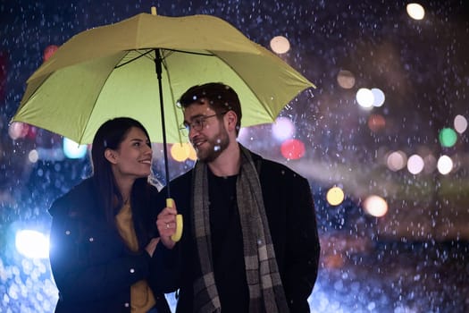 In the romantic ambiance of a rainy night, a happy couple walks through the city, sharing tender moments under a yellow umbrella, surrounded by the glistening glow of urban lights.