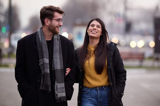 A romantic couple embraces in a tender hug as they stroll through the city streets, enjoying leisure time together in each other's company.