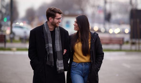 A romantic couple embraces in a tender hug as they stroll through the city streets, enjoying leisure time together in each other's company.