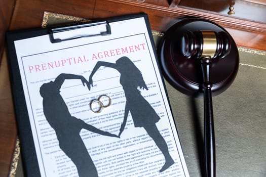 A clipboard holding a prenuptial agreement with a cut-out silhouette of a couple and wedding rings, next to a judge's gavel