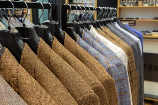 A row of men's suits, jackets hanging on a rack for display. Elegant man suit jackets hanging in a row on hangers.