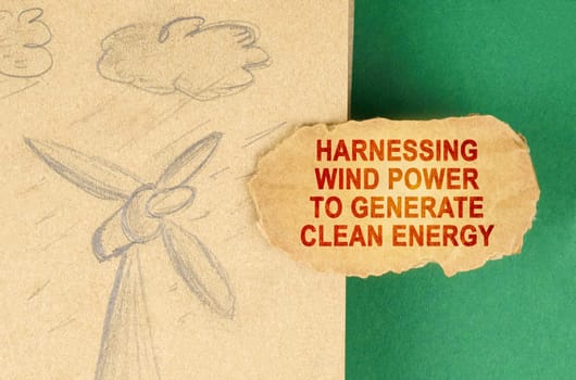 Alternative energy concept. On a green surface there is a drawing with a wind generator and a cardboard with the inscription - Harnessing wind power to generate clean energy