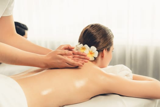 Caucasian couple customer enjoying relaxing anti-stress spa massage and pampering with beauty skin recreation leisure in day light ambient salon spa at luxury resort or hotel. Quiescent