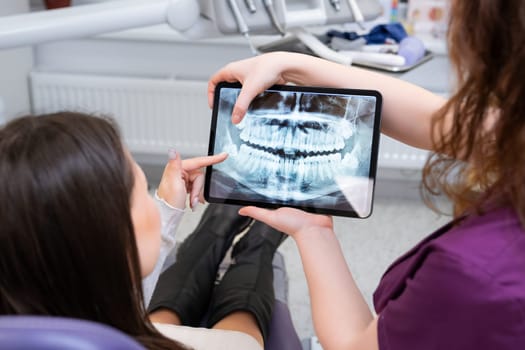 A female dentist discusses treatment strategies with the patient displaying the X ray image on the tablet
