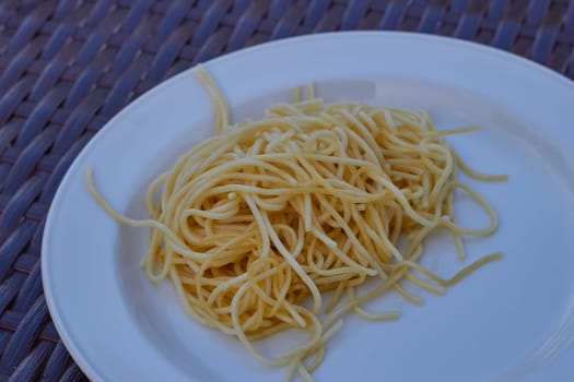 Photo of spaghetti on a white plate on a rattan table. Serving food. Eating. Dinner. Supper.