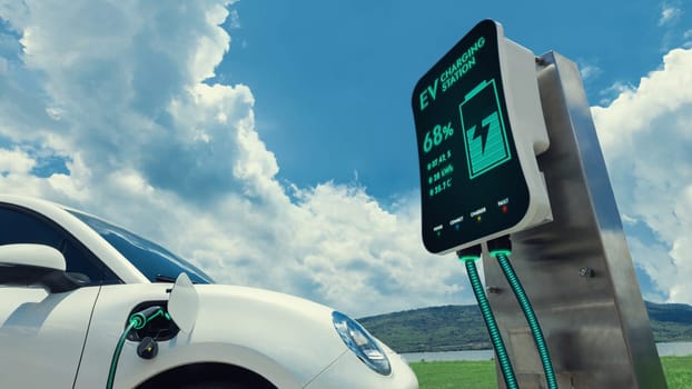 Electric car plugged in with charging station to recharge battery by EV charger cable with nature vacation background. Future innovative ev car and energy sustainability. Peruse