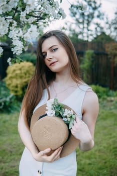 Beautiful young girl in white dress and hat in blooming Apple orchard. Blooming Apple trees with white flowers