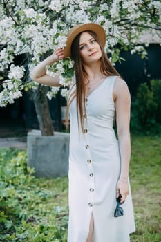 Beautiful young girl in white dress and hat in blooming Apple orchard. Blooming Apple trees with white flowers