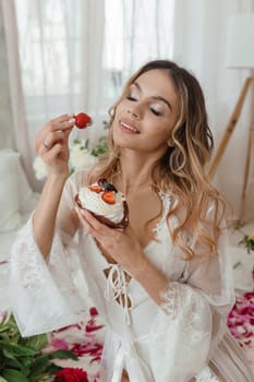 A beautiful girl is eating a strawberry shortcake at home, surrounded by spring flowers on a large bed. A room decorated with bouquets of peonies