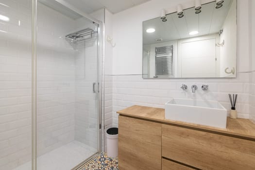 Contemporary bathroom design featuring a glass shower, wooden vanity, and white tiles.