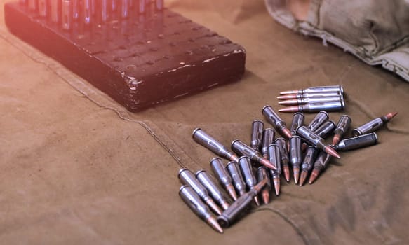 A soldiers hand is carefully reaching into a wooden box to hold a single bullet, while scattered bullets are arranged on an olive drab cloth surface, creating a compelling sense of depth and focus.