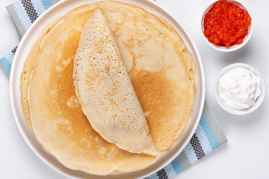 Pancakes with red caviar and sour cream, Close-up of pancakes stacked on white background.