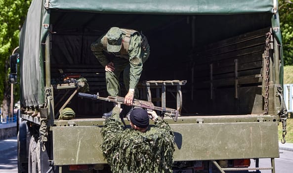 Soldiers unload firearms from a military truck. A soldier in the back of a truck.