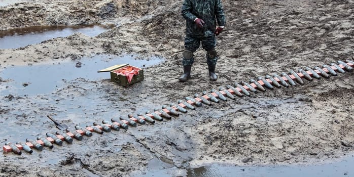 A soldier in uniform prepares weapons in a muddy field, surrounded by ammunition boxes. The low angle shot makes the soldier look powerful and intimidating, capturing the horror and futility of war.