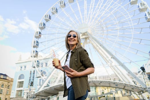 A woman standing in front of a colorful ferris wheel at an amusement park, looking up at the towering structure.