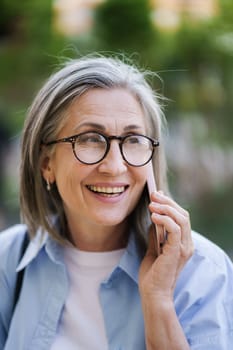 A woman with glasses engaged in a phone call on her cell phone, standing outdoors.