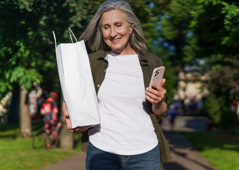 A woman holding a white bag and a cell phone in her hand outdoors.