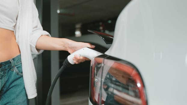 Young motion woman travel with EV electric car to shopping center parking lot charging station in downtown city sustainability lifestyle by green clean rechargeable energy of electric vehicle innards