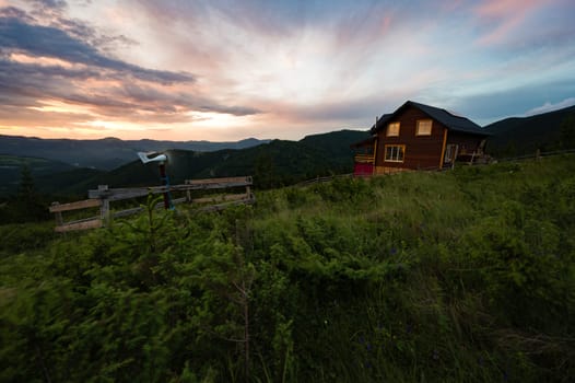 One house in the mountains, in the foreground a small windmill that generates electricity for the house in the mountains.