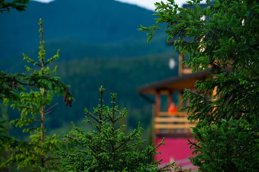 Blurred person silhouette in an orange jacket stands on the terrace of a wooden house against the background of mountains, a house for tourists in the Carpathians of Ukraine.