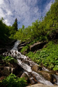 Mountain waterfall on the background of the sky with a summer sunny day, a waterfall in the Carpathians.