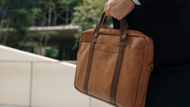 Close up of suitcase was held by profession businessman while project manager walking up stairs or step to new position at green eco city. Happy project manager using travel bag. Focus on bag. Urbane.