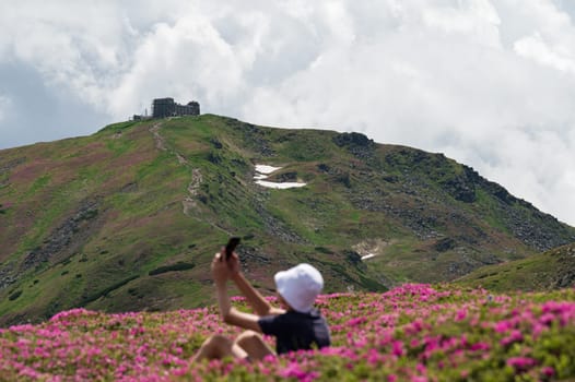 A guy with a white panama on his head sits between rhododendrons with a view of Pip Ivan, summer vacation in the Carpathians.