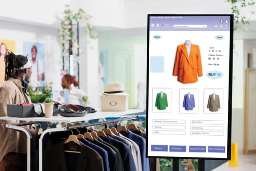 Interactive monitor board kiosk service, trendy clothing items and merchandise on display in fashion boutique at mall. Touch screen with user interface of online shop, self service checkout.