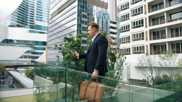 Caucasian business man hold mobile phone and looking at skyscraper view. Skilled male leader standing rooftop in modern building. Caucasian executive manager look at phone while rest his eyes. Urbane.