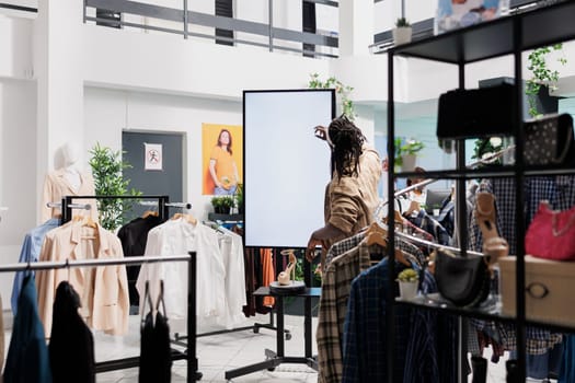 Customer pressing on smart whiteboard touch screen in clothing department shop. African american man using interactive board with blank display to read about female shoes in fashion store