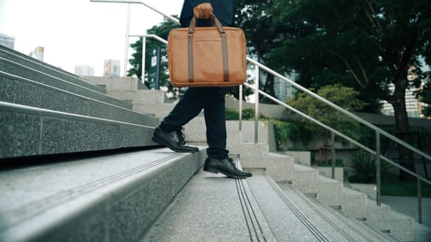 Closeup imaged of smart business man leg walking while holding a bag for working. Project manager going down to stairs for working. Represented transportation, traveling. Focus on leg. Exultant.