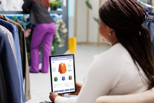 Boutique client using clothing store app on digital tablet, looking at online website to buy modern fashion line. Female buyer doing shopping on mobile application, trendy clothes shop.