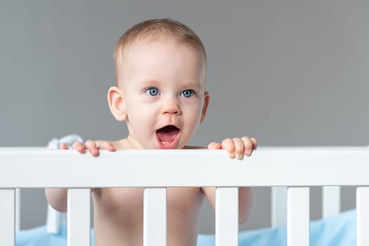 Portrait of one year old baby standing in a crib smiling