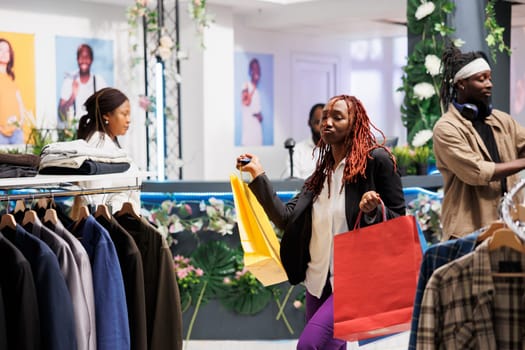 Satisfied customer carrying shopping bags and dancing in clothing store. Happy african american woman shopaholic buying new apparel with discount and holding packages in fashion boutique