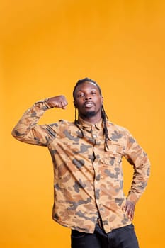 Portrait of athletic bodybuilder showing trained arm muscles in front of camera in studio over yellow background. African american man enjoying sport exercices, working out at triceps strength.