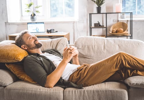 A man laying down on a couch with a pillow placed on his back.