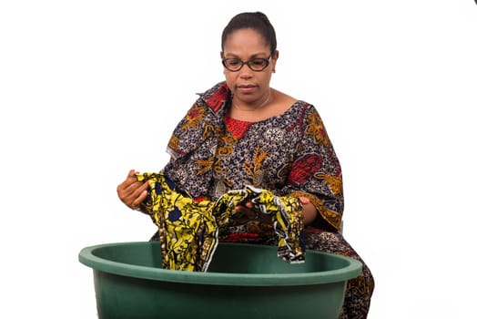 mature african woman in loincloth sitting doing laundry.