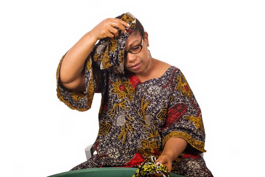 African woman sitting and washing clothes in a big green bowl while arranging her scarf over her head isolated on white background.