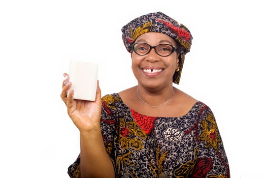 Happy woman dressed in african outfit with scarf on head holds and presents white soap to camera with hand gesture isolated on white background.