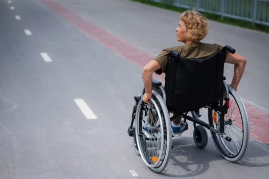 Rear view of an elderly woman in a wheelchair riding on a bike path