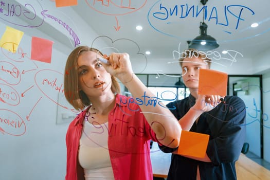 Couple of young creative start up business people brainstorming idea and solving problems by using sticky note and mind map at glass board, meeting room. discussing, working together. Immaculate.