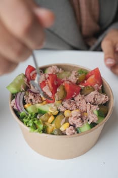 spoon pick tuna salad from a bowl on table .