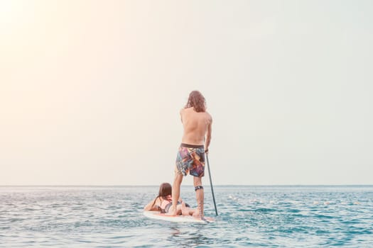 Sea woman and man on sup. Silhouette of happy young woman and man, surfing on SUP board, confident paddling through water surface. Idyllic sunset. Active lifestyle at sea or river