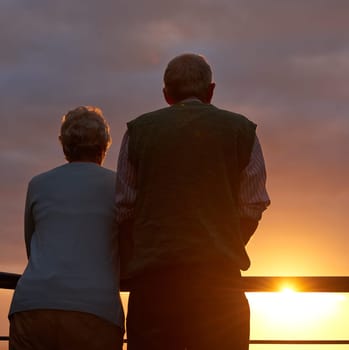 Senior couple, sunset and together on balcony in outdoors, bonding and love on vacation or holiday. Back, elderly people and dusk on terrace and together in nature, security and travel for marriage.