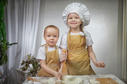 Cute oriental family with small brother and sister cooking in the kitchen on Ramadan, Kurban-Bairam, Eid al-Adha. Funny children boy and girl at cook photo shoot. Pancakes, Maslenitsa, Easter